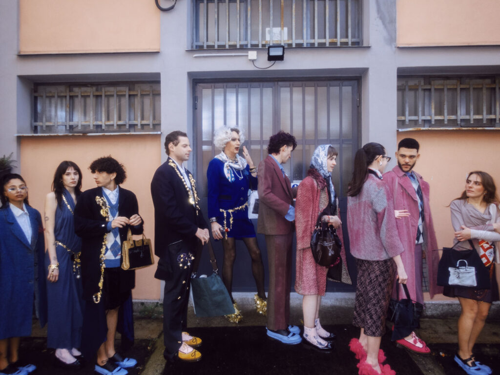 A scene featuring a group of fashionably dressed individuals standing in line outside a building.